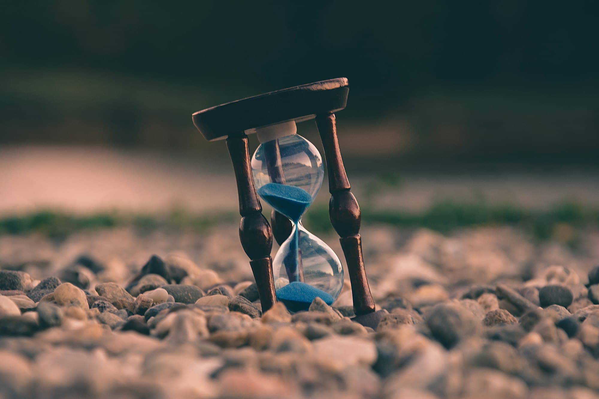 An hourglass with blue sand standing on pebbles
